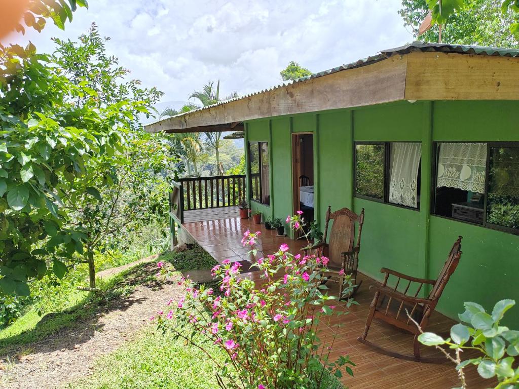 a green house with a porch and some flowers at Bella Vista Guest house in Turrialba