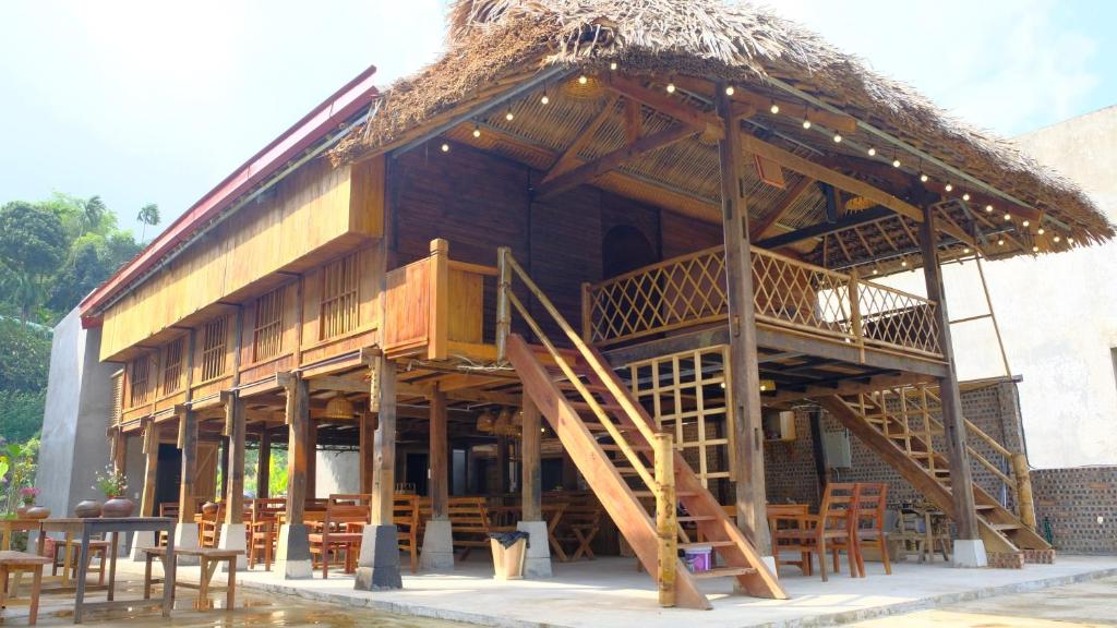 un edificio con tetto di paglia, tavoli e sedie di HÀ GIANG WOODEN HOUSE a Ha Giang