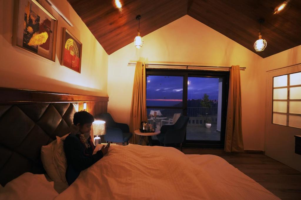 une personne assise sur un lit dans une chambre avec fenêtre dans l'établissement Hotel Evara, à Mussoorie