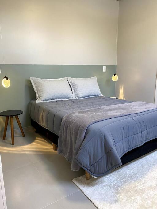 a bedroom with a bed with a blue blanket and a table at Loft 116 B - Porto Belo/SC in Porto Belo