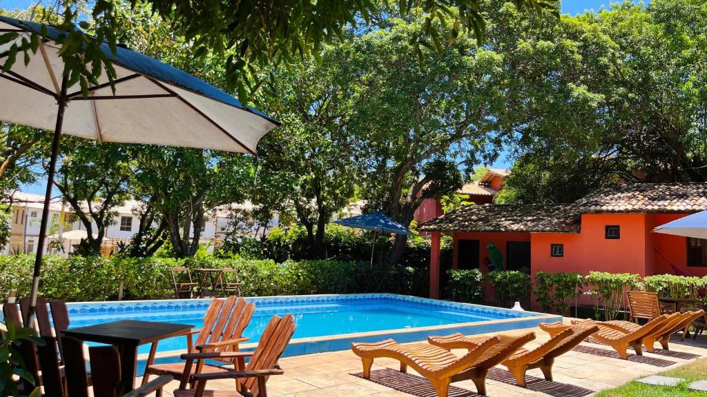 einen Pool mit Stühlen, einem Tisch und einem Sonnenschirm in der Unterkunft Pousada Canto do sabiá Imbassaí in Imbassai