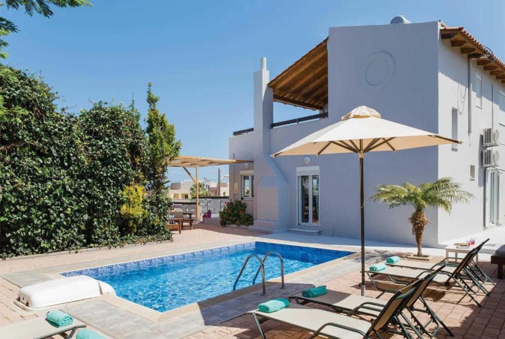 einem Pool mit Stühlen und einem Sonnenschirm neben einem Haus in der Unterkunft Villa Rea in Adelianos Kampos