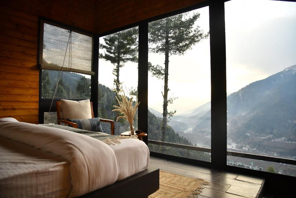 a bedroom with a large window with a mountain view at Montane Chalet , Sethan in Manāli