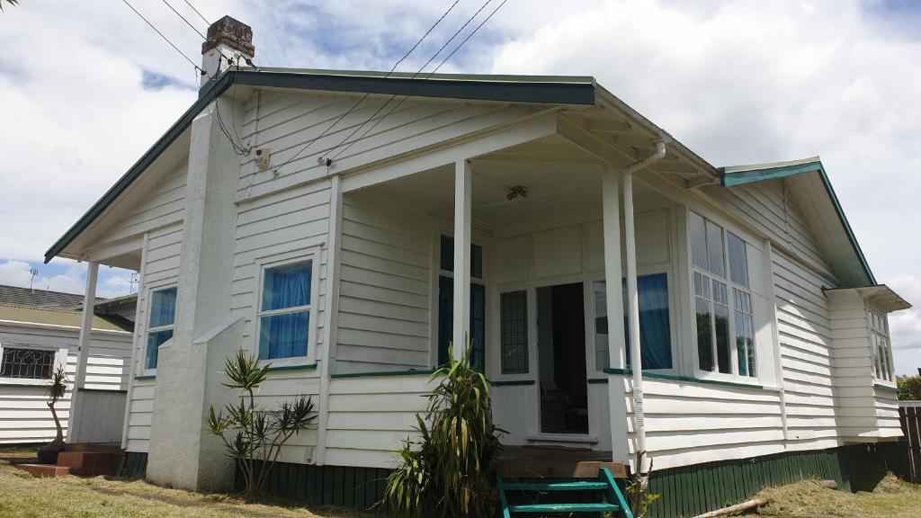a small white house with a porch at Green Getaway- Unique, 4 bedroom Bungalow Papakura in Auckland