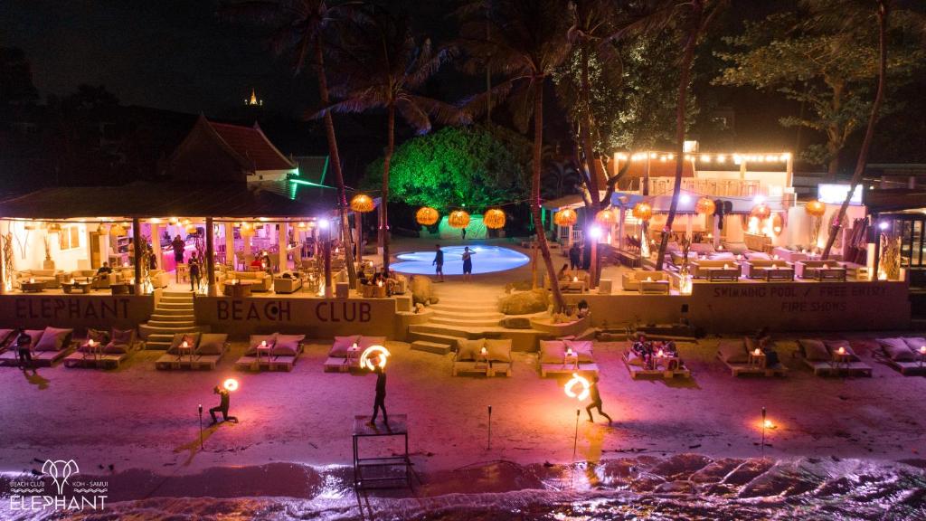 Elephant Beach Club & Resort Samui في شاطئ تشاوينغ: وجود نادي شاطئي في الليل مع الكراسي والأضواء