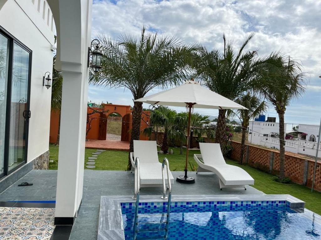 a patio with two chairs and an umbrella and a pool at Emirate Villa Mui Ne in Mui Ne