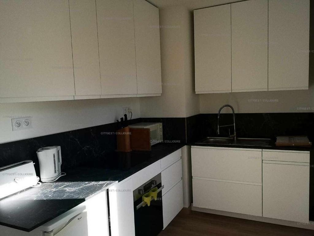 a kitchen with white cabinets and black counter tops at 4PA72 - Magnifique appartement pour 4 dans résidence avec piscine et parking in Collioure