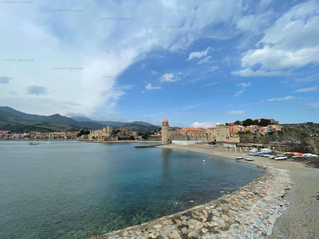 a beach with a town and a lighthouse in the water at 4PA72 - Magnifique appartement pour 4 dans résidence avec piscine et parking in Collioure
