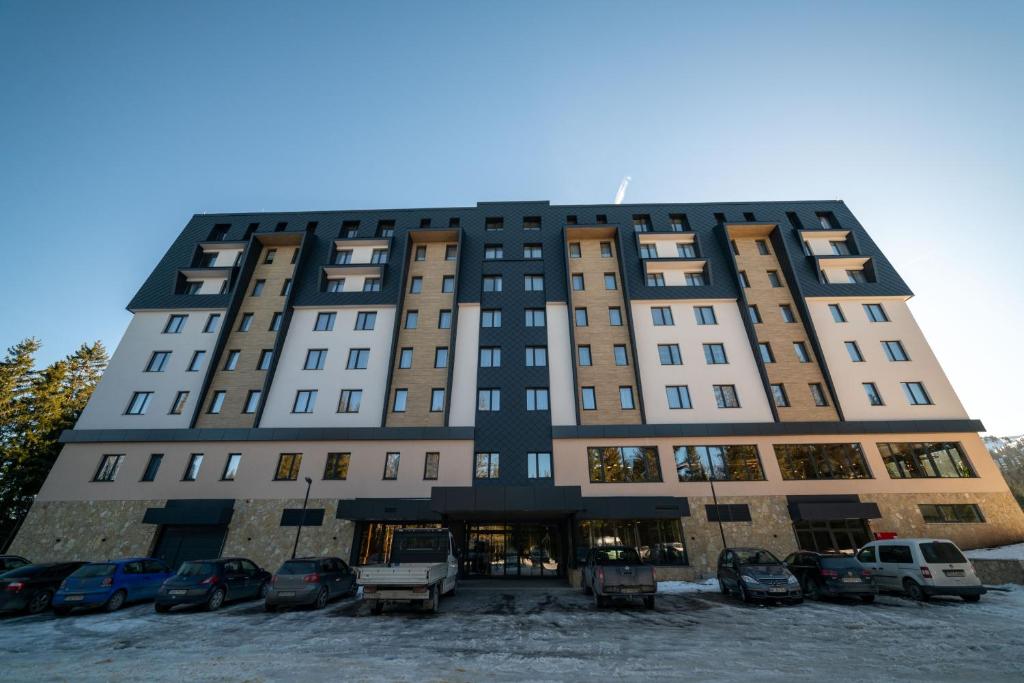 a large building with cars parked in a parking lot at Lux apartment Zlatni Javor Jahorina in Jahorina