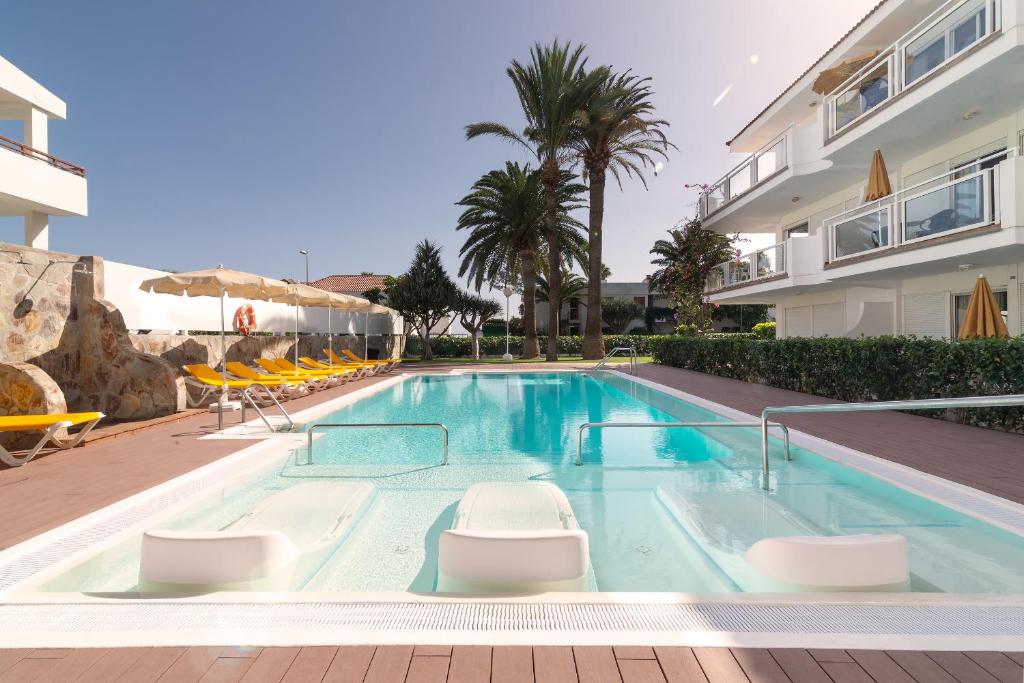 a swimming pool with chairs and a building at Apartamentos Montemayor in Playa del Ingles