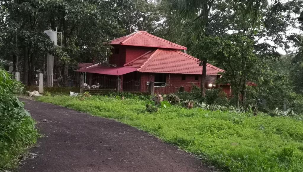 a red house with a red roof on a road at Sarvoday Eco Homestay, Sawantwadi in Sawantwadi