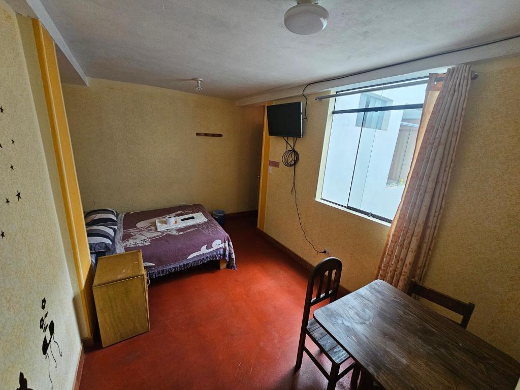 um pequeno quarto com uma cama, uma mesa e uma janela em HOSTAL DALIA em Chivay