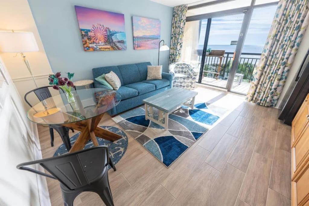 a living room with a blue couch and a glass table at Your Beachfront Resort Oasis in Myrtle Beach