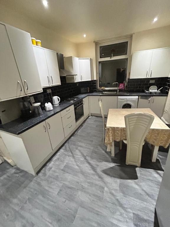 cocina con armarios blancos, mesa y sillas en 40 vicarage street en Failsworth