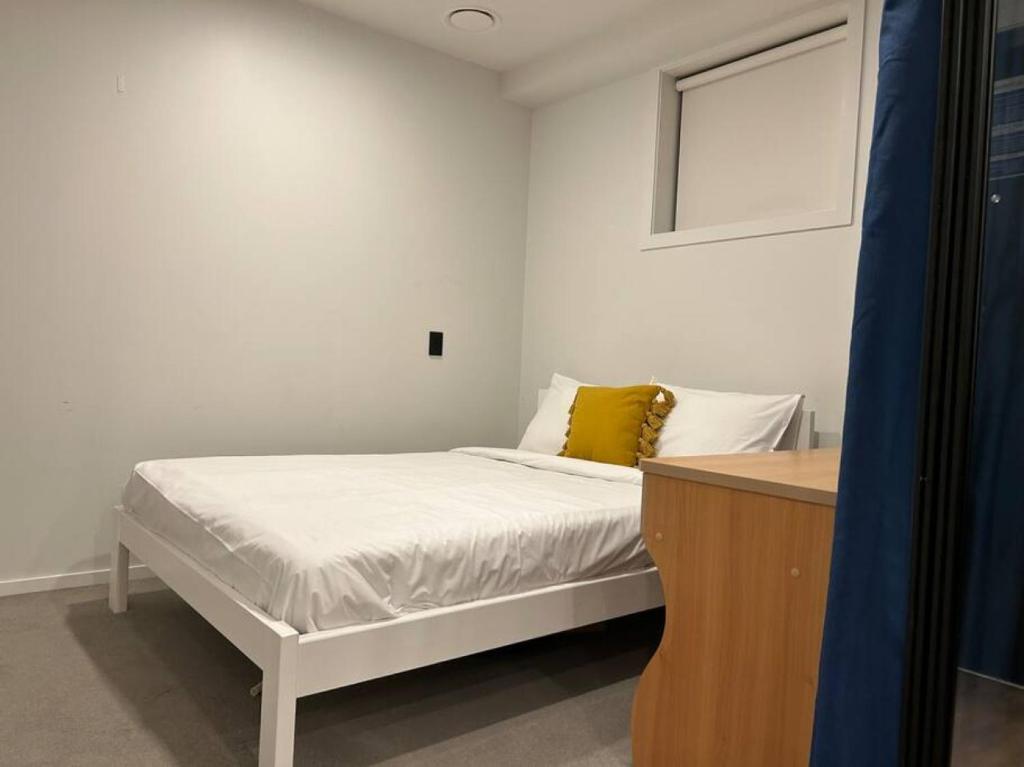 een witte slaapkamer met een bed met een geel kussen bij Top Floor Vincent in Auckland