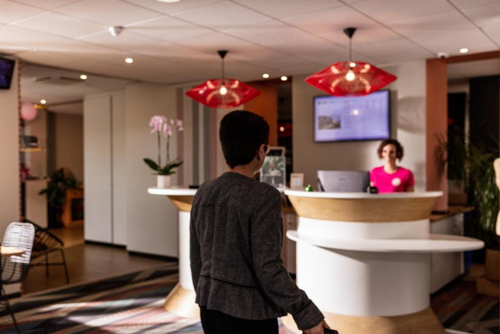 a young man walking through a lobby with a woman at a counter at ibis Styles Toulouse Lavaur in Lavaur
