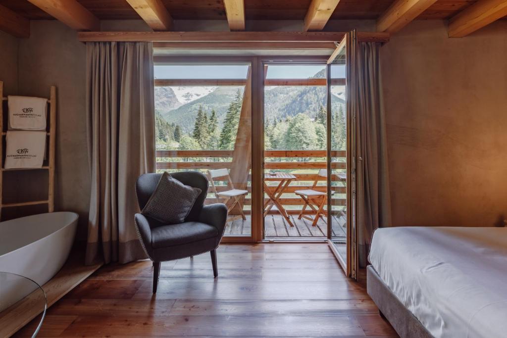 a bedroom with a tub and a chair and a balcony at Au Charmant Petit Lac - Ecohotel Parc & Spa in Champoluc