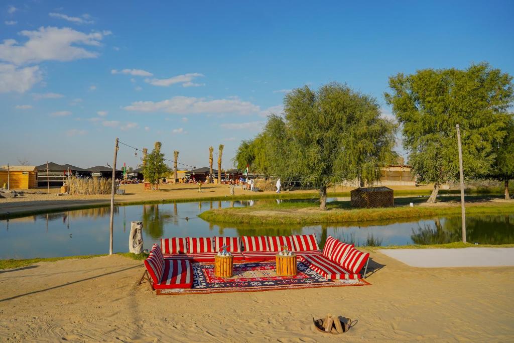 Al Marmoom Oasis “Luxury Camping & Bedouin Experience” في دبي: كنب احمر جالس على الرمال في حديقه