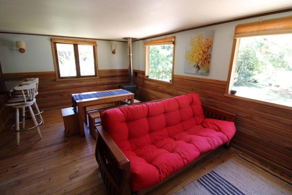 ein rotes Sofa in einem Zimmer mit Holzwänden in der Unterkunft TuArriendoCL-Acogedora Cabaña Cercana a Playa Niklitschek hasta 5 PAX in Puerto Varas