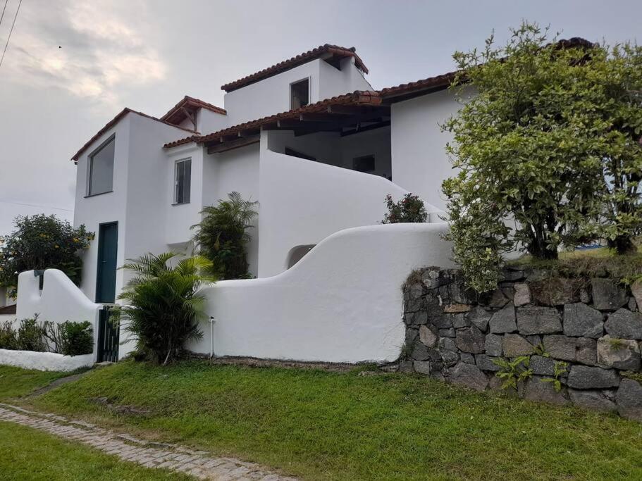 a white house with a stone wall at Casa Grega em Angra dos Reis com Piscina e Vista Espetacular in Angra dos Reis