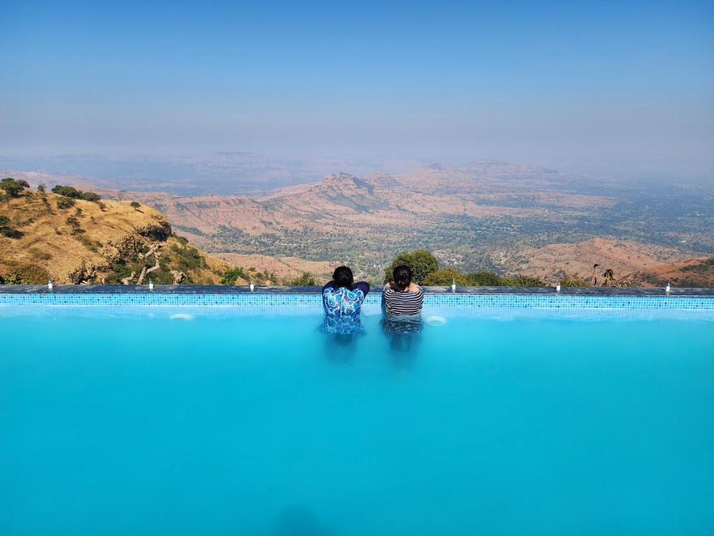 dos mujeres sentadas sobre un gran cuerpo de agua en Hilltop Resort and Agro Tourism Wai, Near Panchgani en Wai