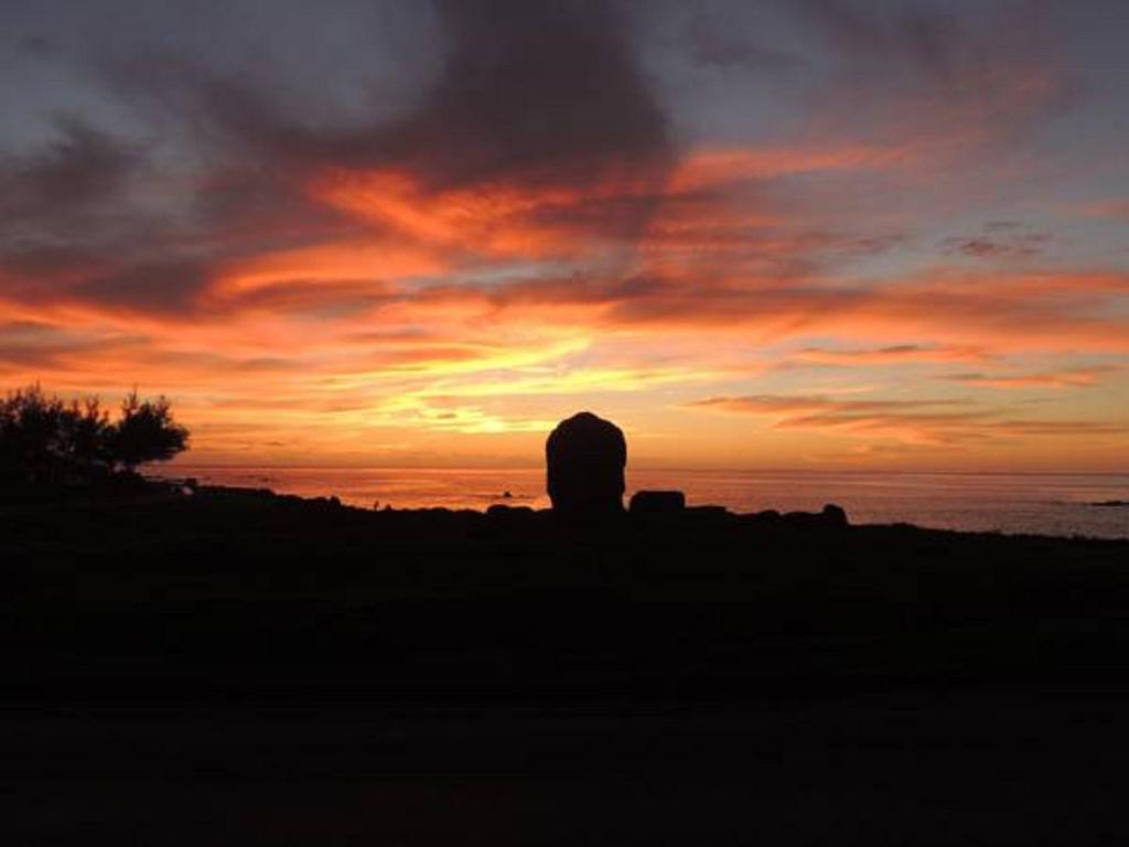 einen Sonnenuntergang am Strand mit dem Ozean im Hintergrund in der Unterkunft Ngahu Bungalows Alojamiento Frente al Mar en el centro de Rapa Nui in Hanga Roa