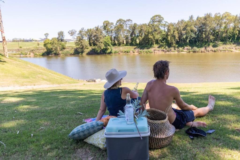 two people sitting on the grass next to a lake at Pitt Town Ferry Park in Wilberforce