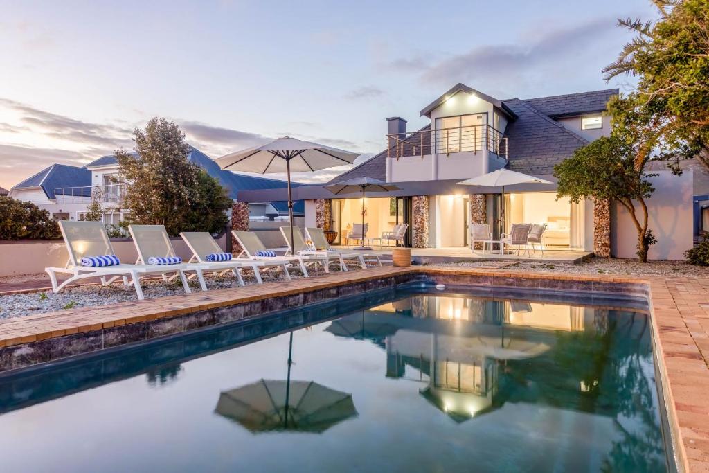 a home with a swimming pool with chairs and a house at 38 on Westcliff in Hermanus