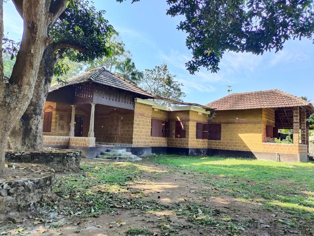 une vieille maison avec un arbre en face dans l'établissement Chithira Homestay (Kerala traditional mud house), à Kodali