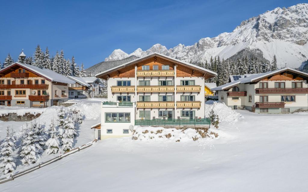 a building in the snow with mountains in the background at Aparthotel Sunrise in Ramsau am Dachstein