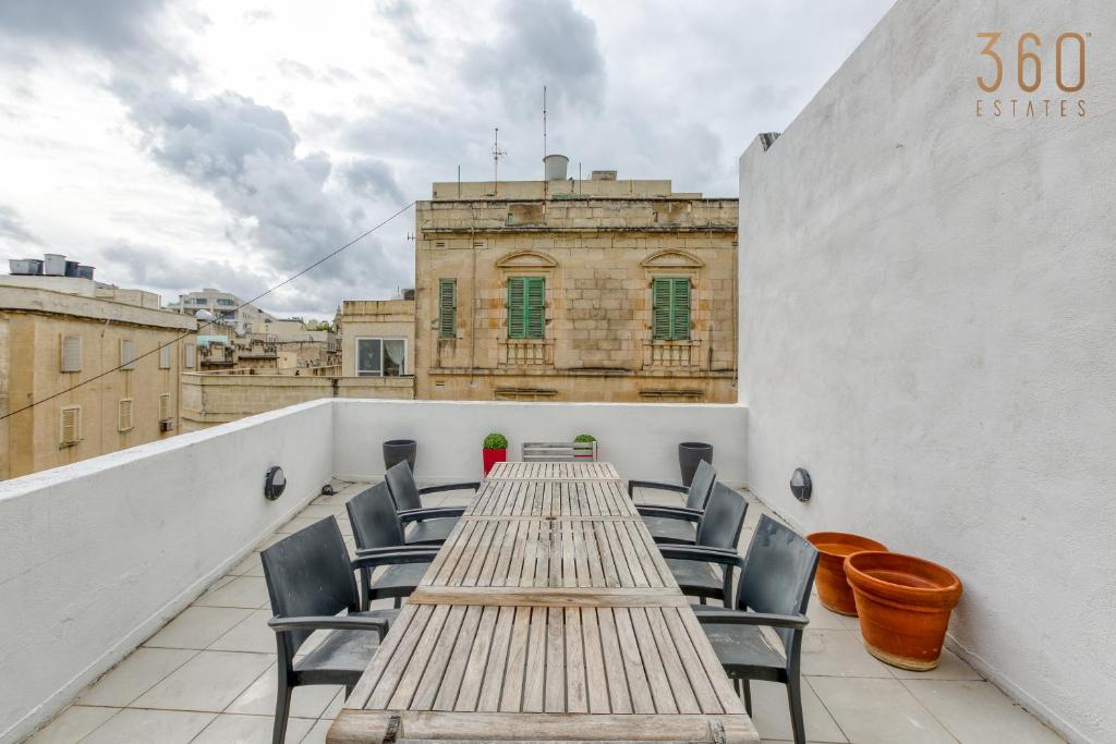 einen langen Holztisch und Stühle auf dem Balkon in der Unterkunft An amazing 2BR home with a special private rooftop by 360 Estates in Sliema