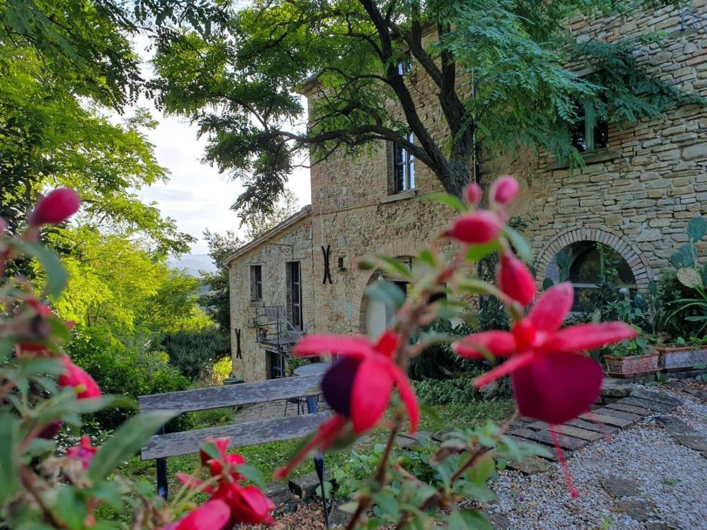 Antico-Borgo-Le-Torricelle-Grosses-Haus في Piandimeleto: مقعد أمام مبنى من الطوب عليه زهور حمراء