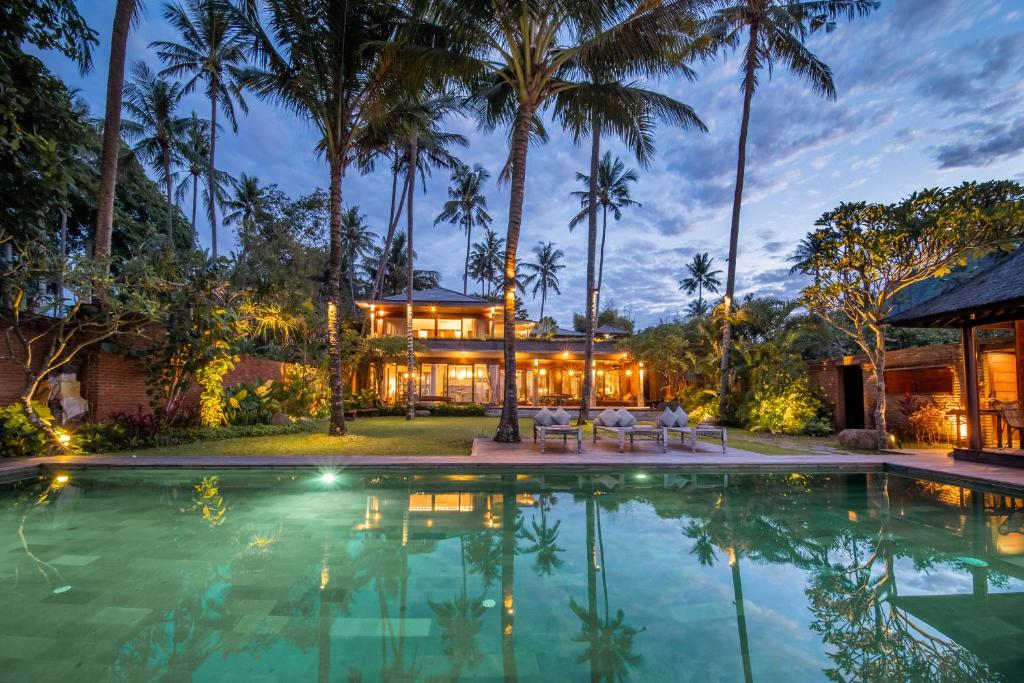 a house with a swimming pool and palm trees at Villa Manis Beachfront Candidasa in Candidasa