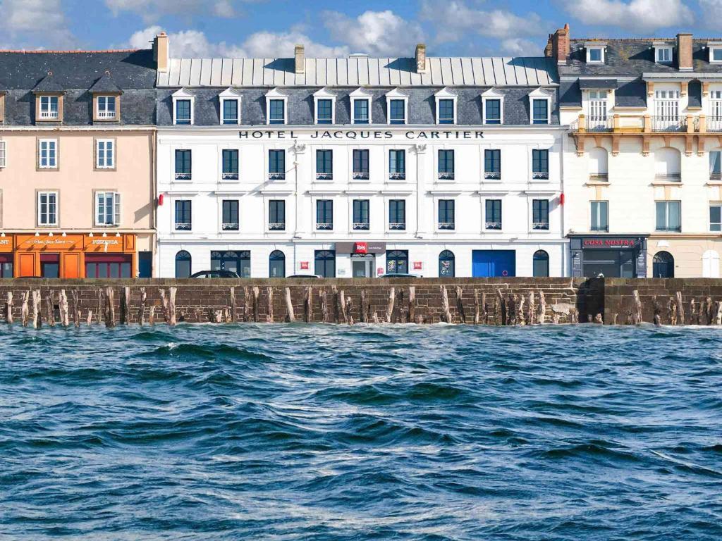 a building next to the water in front of a pier at ibis Saint Malo Plage in Saint Malo