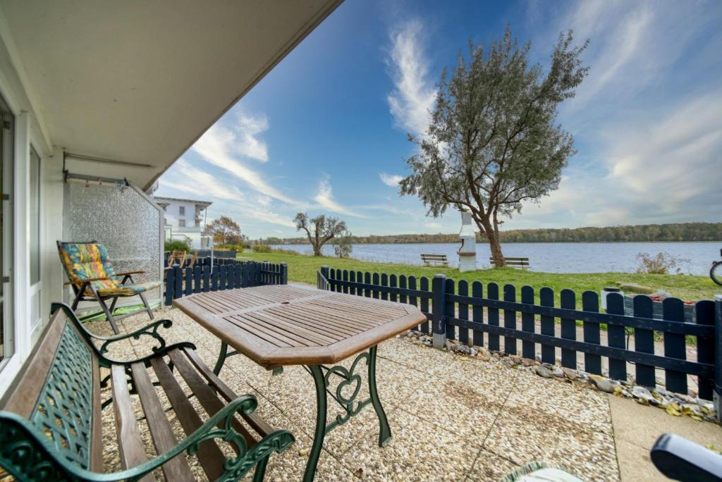 einen Tisch und eine Bank auf einer Veranda mit Blick auf das Wasser in der Unterkunft Haus am See, App 3HAS06 in Heiligenhafen