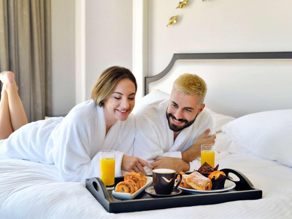 a man and woman sitting in bed with a tray of food at Mövenpick Hotel Bahrain in Manama