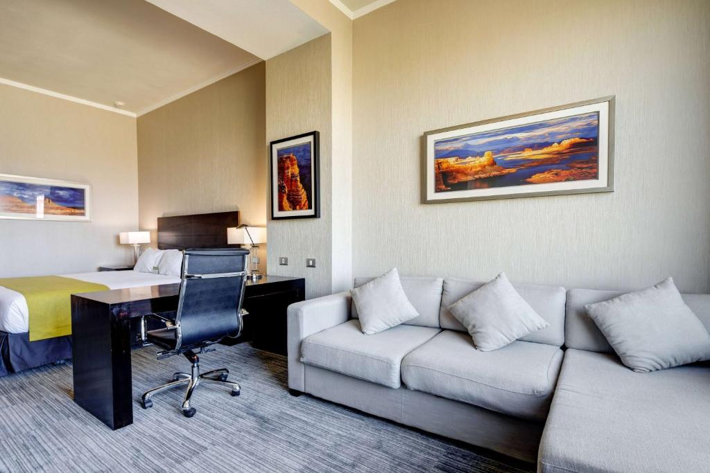 a hotel room with a couch and a desk and a bed at La Quinta by Wyndham Santiago Aeropuerto in Santiago
