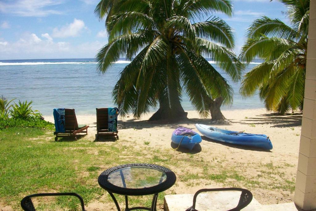 Vaiakura Holiday Homes في راروتونغا: شاطئ يوجد به كراسي وقوارب الكاياك والنخيل