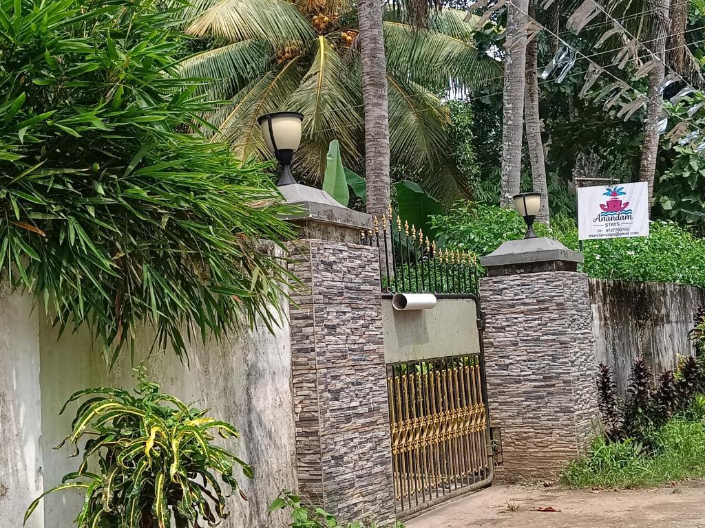 a gate in a brick wall with palm trees at Anandam Woods - A Heritage single Room for couple-small family in Vaikom