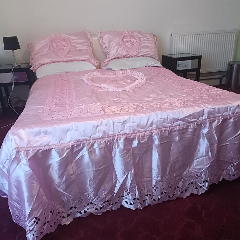 a pink bed with a pink comforter and pillows at Alysguesthub in London