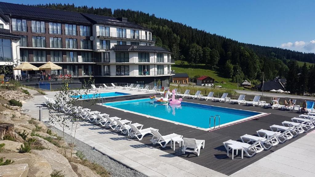 ein Hotel mit einem Pool mit Stühlen und einem Resort in der Unterkunft Czarna Perła - Czarna Góra Resort by Sun & Snow z nielimitowanym basenem in Heudorf
