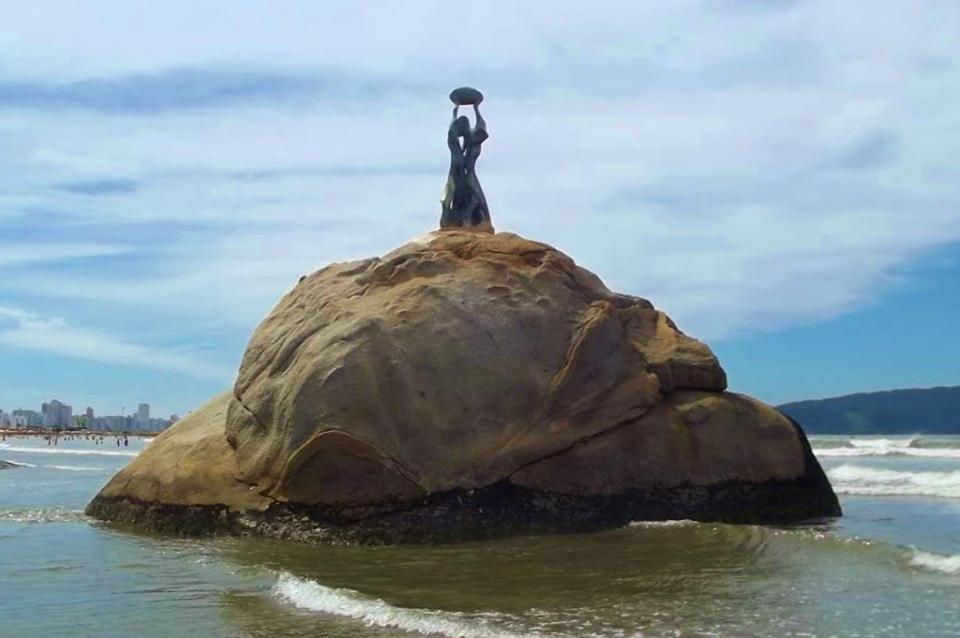 une personne debout sur un rocher dans l'océan dans l'établissement Apartamento na Praia de Itararé, à São Vicente