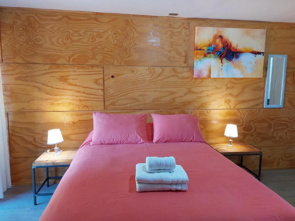 um quarto com uma cama vermelha com lençóis cor-de-rosa e 2 candeeiros em Verdevida Apart Hotel em Pucón