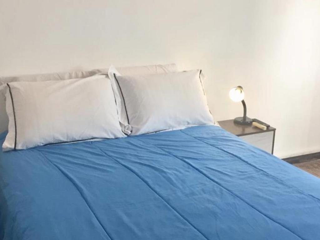 a blue bed with white pillows and a table with a lamp at Artistes du Monde in Montevideo