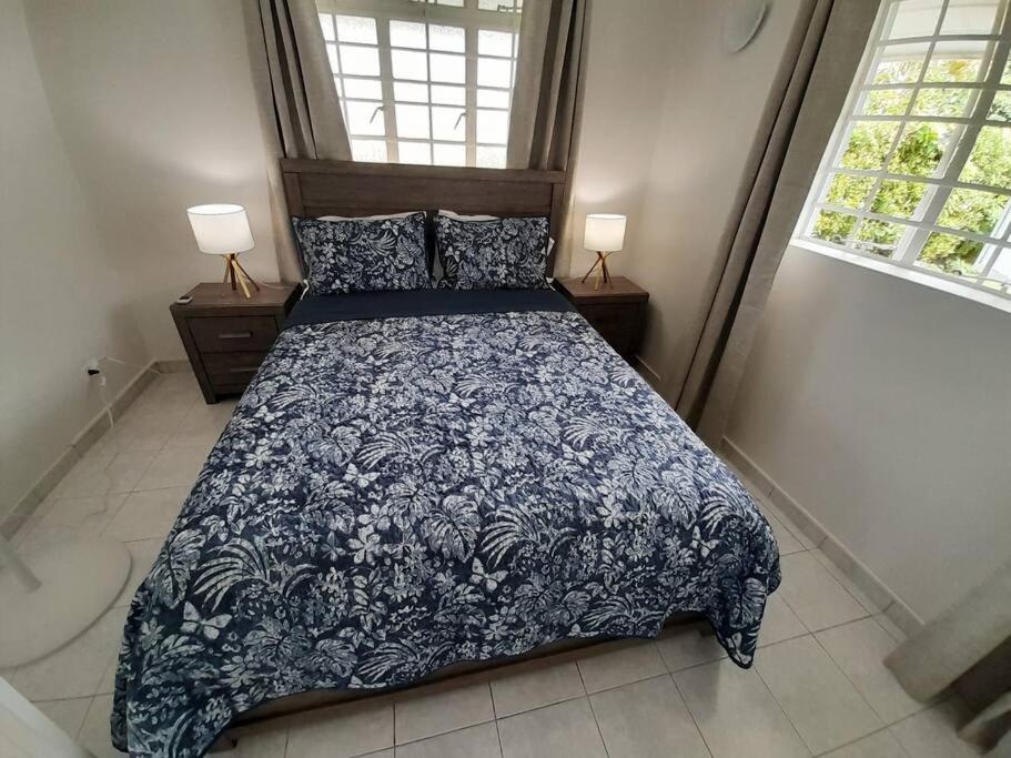 a bedroom with a bed with a blue bedspread and two windows at Apt 1 Lynsted - Newly renovated 2 bed 1 bath in Bridgetown
