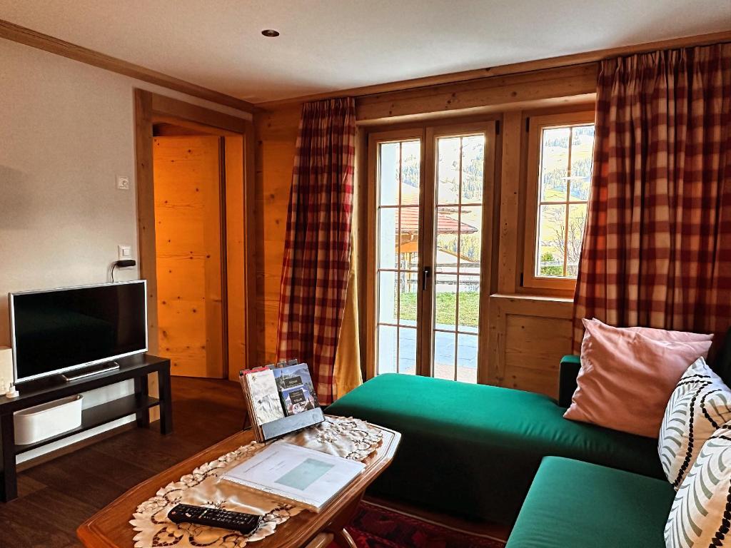 un salon avec un canapé vert et une télévision dans l'établissement One Bedroom with mountain and garden view ground floor of Chalet Solaria, à Zweisimmen