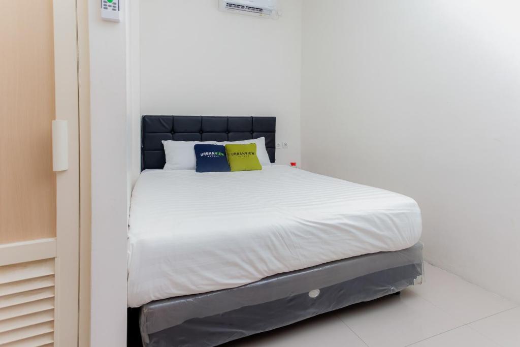 1 cama con sábanas blancas y almohadas azules y amarillas en Urbanview Hotel Priority Samarinda by RedDoorz en Samarinda