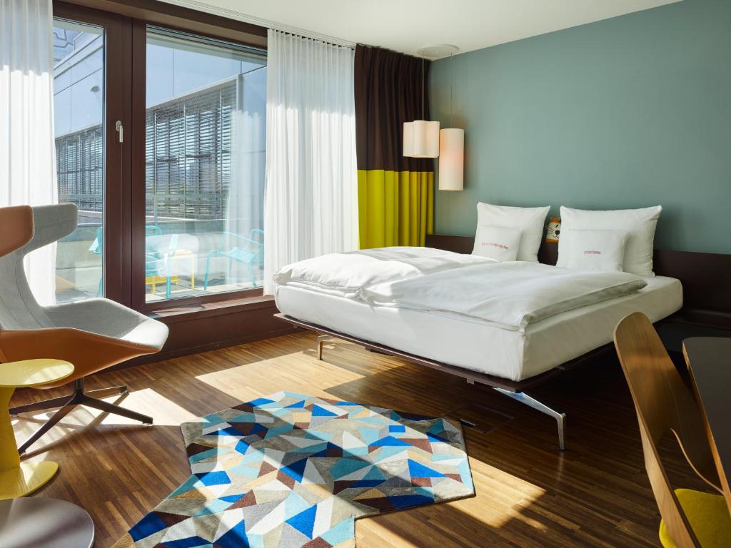 a bedroom with a bed and a chair and a window at 25hours Hotel Zürich West in Zürich