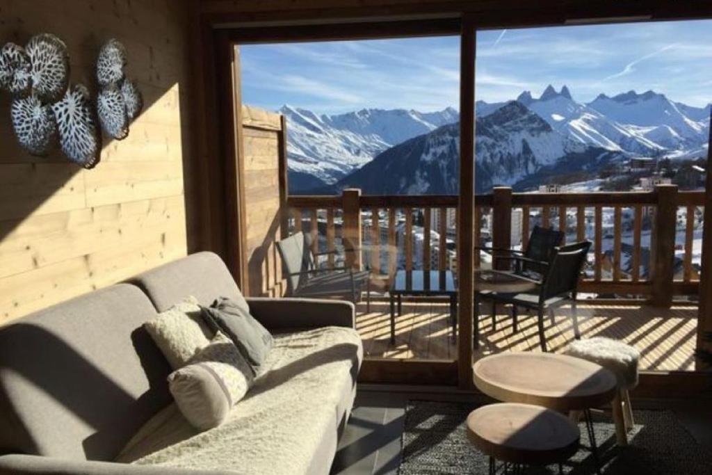 a living room with a couch and a balcony with mountains at LOdyssée 203 in La Toussuire
