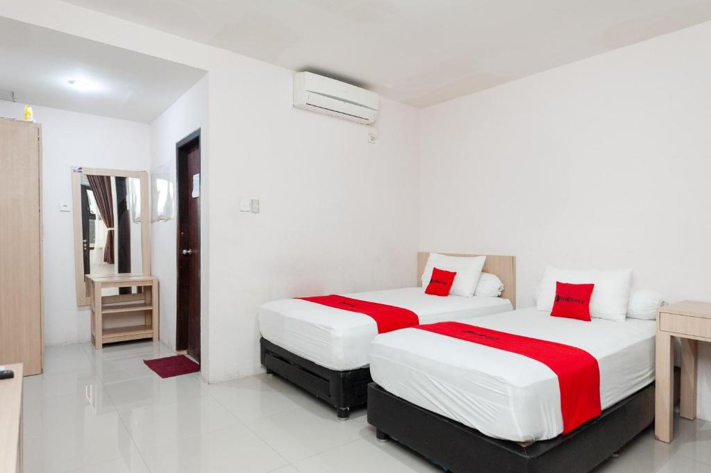 Duas camas num quarto com paredes brancas e almofadas vermelhas em RedDoorz Syariah near Banda Aceh Convention Hall em Lamnyong